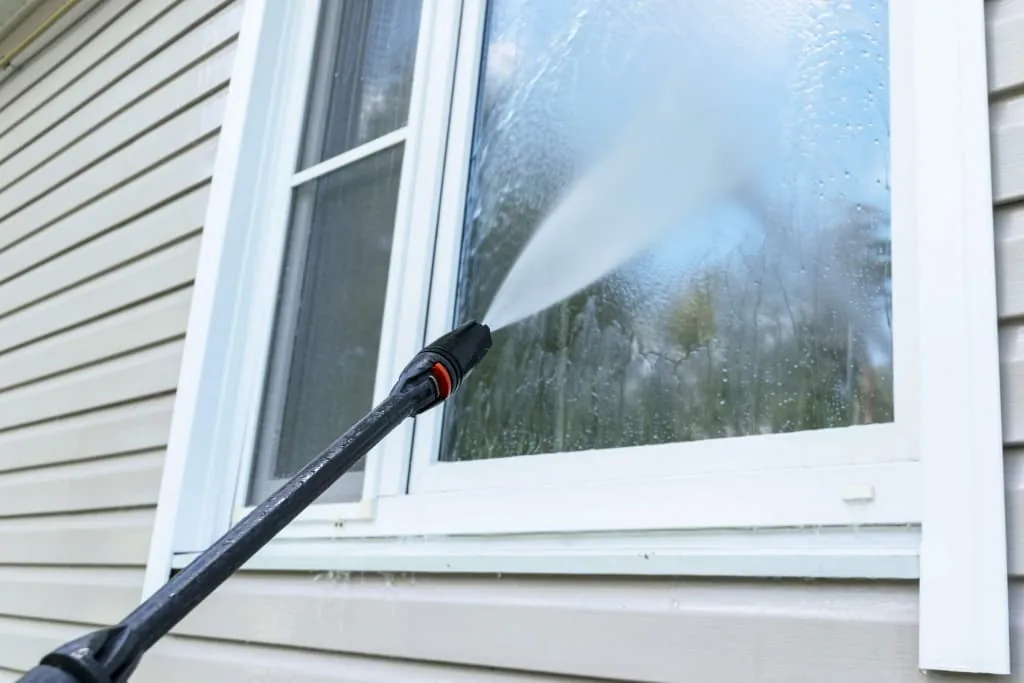 Pressure washing a home's exterior window and siding with a high-pressure spray
